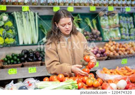 Young female shopper selects and buys tomatoes in supermarket 120474320