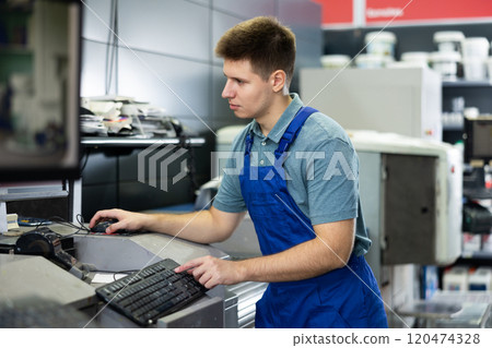 Man in uniform operating computerised machne to mix paint Man in uniform operating computerised machne to mix paint 120474328