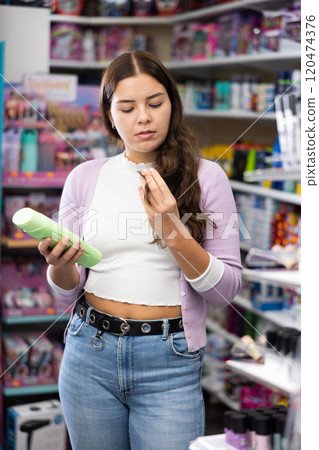 Portrait of positive woman looking on modern mousse for her hair in store. Portrait of positive woman looking on modern mousse for her hair in store. 120474376