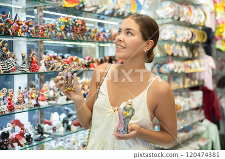 Female tourist happily chooses various souvenir figurines in spanish souvenir shop Female tourist happily chooses various souvenir figurines in spanish souvenir shop 120474381