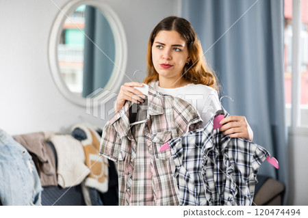 Young woman chooses what shirt to wear in the interior of house 120474494