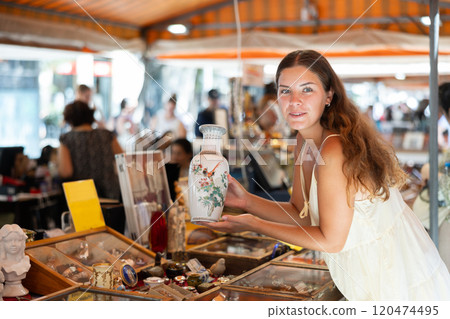 Girl in flea market store look at Chinese porcelain painted vase, antique gifts 120474495