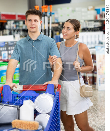 Positive young couple with trolley planning to make house renovation talking with interest and looking for paints, varnishes and tools in store Positive young couple with trolley planning to make house renovation talking with interest and looking for paints, varnishes and tools in store 120474583