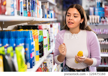 Portrait of positive female buying hair conditioner or mousse in hair care products shop Portrait of positive female buying hair conditioner or mousse in hair care products shop 120475160