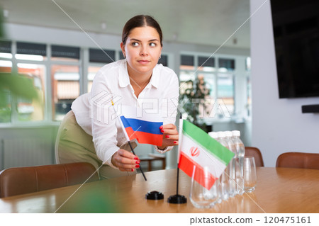 Positive young woman putting little flag of Russia on table next to the flag of Iran 120475161
