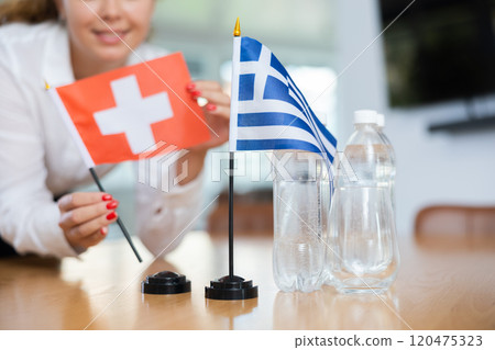 Unrecognizable girl sets midget flags of Greece and Switzerland before international negotiations Unrecognizable girl sets midget flags of Greece and Switzerland before international negotiations 120475323