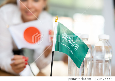 Little flag of Saudi Arabia on table and flag of Japan put next to it by young woman 120475338