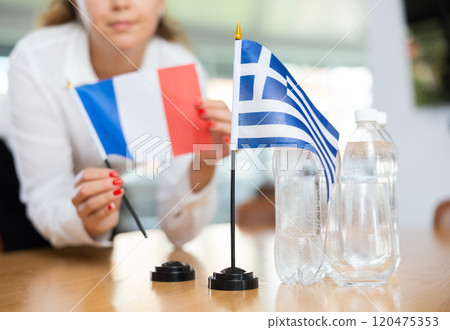 Unrecognizable girl sets midget flags of Greece and France before international negotiations 120475353