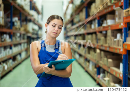In warehouse of store, girl checks quantity of goods and receipt documents for products 120475432