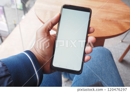 A person sits in a cozy cafe, holding a smartphone with a blank screen, hinting at engagement 120476297