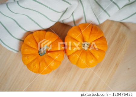 Two bright orange pumpkins rest on a rustic wooden surface with a linen cloth draped beside 120476455