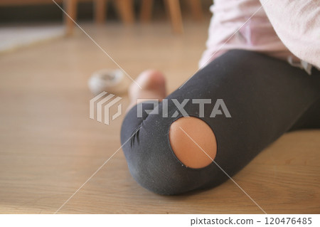 Close-Up of Worn-Out Leggings with Ripped Knee on Wooden Floor 120476485