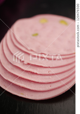 Slices of Pink Bologna Featuring Green Specks Presented Against a Dark Background 120476500