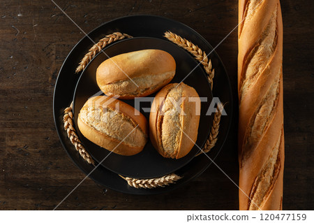 Baguette, French buns, and wheat ears on an old wooden table. 120477159