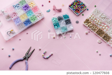 Crafting beautiful jewelry with beads and supplies on a pastel pink surface Crafting beautiful jewelry with beads and supplies on a pastel pink surface 120477608