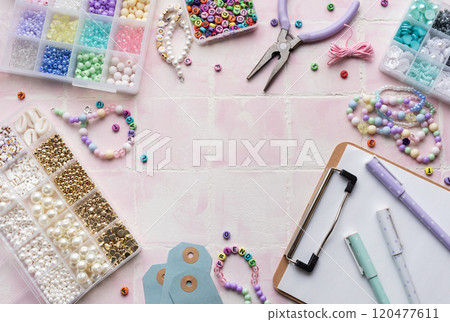 Colorful beads and jewelry making supplies arranged on pink tile background with clipboard and pens Colorful beads and jewelry making supplies arranged on pink tile background with clipboard and pens 120477611
