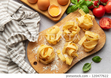 Uncooked tagliatelle pasta nests with basil, tomatoes and eggs on wooden cutting board Uncooked tagliatelle pasta nests with basil, tomatoes and eggs on wooden cutting board 120477622