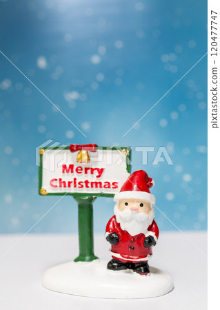 Miniature Santa Claus figurine standing next to a festive Merry Christmas sign 120477747