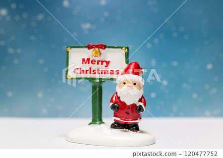 Miniature Santa Claus figurine standing next to a festive Merry Christmas sign 120477752