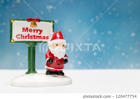Miniature Santa Claus figurine standing next to a festive Merry Christmas sign 120477754