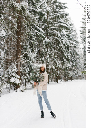 Young woman is standing in snow with scarf wrapped around her neck and hat on her head. She is holding bouquet of flowers cotton Young woman is standing in snow with scarf wrapped around her neck and hat on her head. She is holding bouquet of flowers cotton 120479362