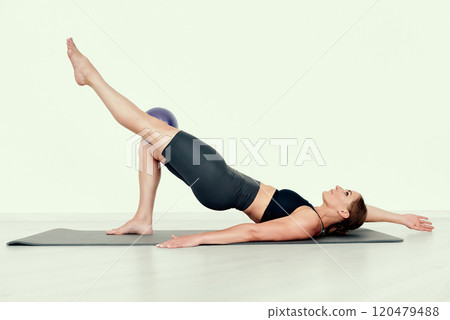 Fitness Trainer Performing Single-Leg Glute Bridge with Ball 120479488