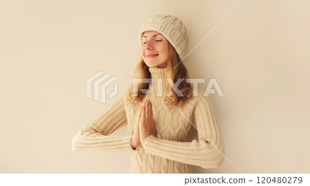 Portrait of relaxed young woman meditates in yoga position closed eyes winter sweater and hat 120480279