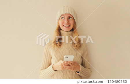 Portrait happy smiling young woman with phone in winter hat, white sweater, girl holding smartphone 120480280