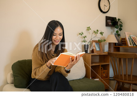 Pretty young woman relaxing in her living room and reading book Pretty young woman relaxing in her living room and reading book 120480818