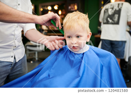 Cute boy getting stylish haircut. Hairdresser in process. Little client first time in barbershop. Cute boy getting stylish haircut. Hairdresser in process. Little client first time in barbershop. 120481580