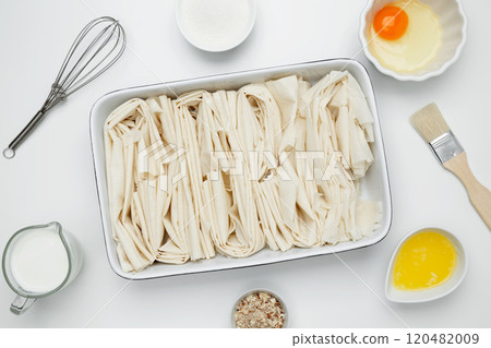 Filo dough in a baking dish near milk, eggs, butter, butter, sugar for Crinkle Cake baking 120482009