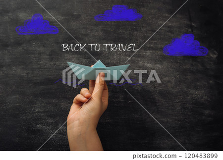 Hand holding a paper boat on a chalkboard with the words Back to Travel Hand holding a paper boat on a chalkboard with the words Back to Travel 120483899