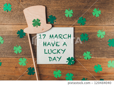 Green shamrock hat is on a wooden surface with a piece of paper 120484040