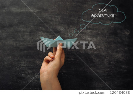 Hand holding a paper boat with the words Sea Adventure written above it 120484088