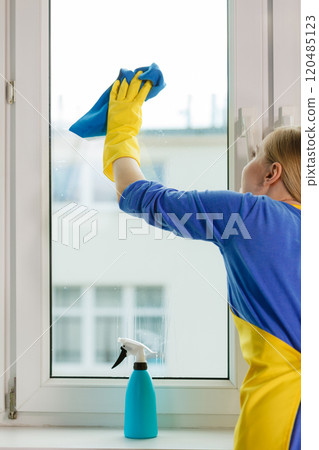Girl cleaning window at home using detergent rag 120485123
