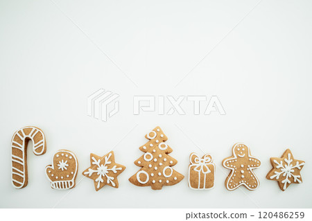 Row of festive gingerbread cookies decorated with white icing, including a candy cane, mitten, snowflakes, Christmas tree, gift box, and gingerbread man, arranged on a white. Row of festive gingerbread cookies decorated with white icing, including a candy cane, mitten, snowflakes, Christmas tree, gift box, and gingerbread man, arranged on a white. 120486259