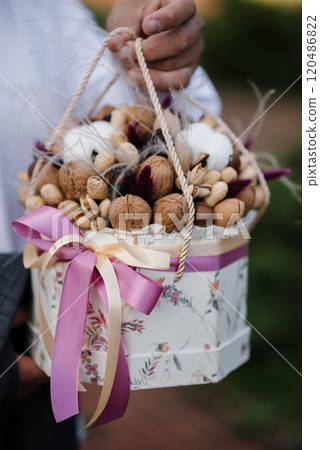 A person is holding a box filled with nuts and flowers 120486822