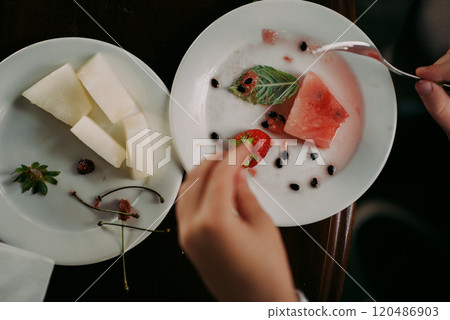 An individual is enjoying a delicious plate of assorted fruit with a fork 120486903