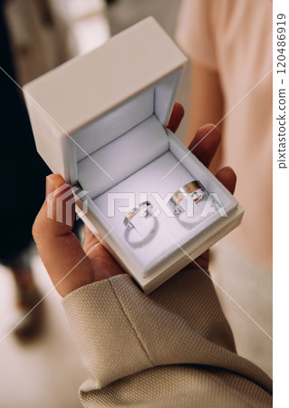 A person is holding a small box with two wedding rings inside 120486919