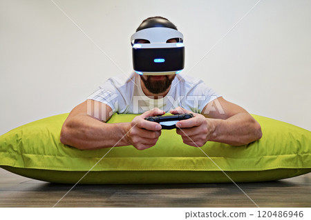 Man lying on green bean bag, fully immersed in VR gaming session with controller Man lying on green bean bag, fully immersed in VR gaming session with controller 120486946