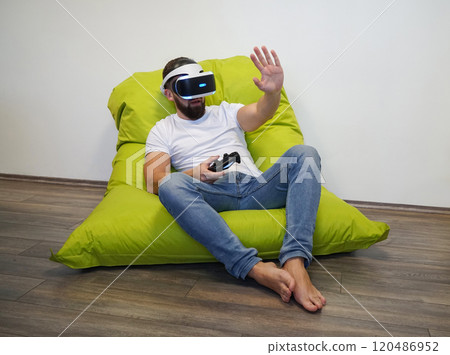 Man is seated on green bean bag, using VR headset and holding controller Man is seated on green bean bag, using VR headset and holding controller 120486952