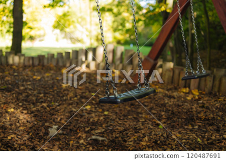Empty black swing on children playground in the park in autumn season. Missing child. Lonely swing in sunny autumn day. Golden foliage in late fall. Beautiful nature.  120487691