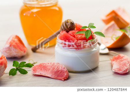homemade sweet yogurt in a glass jar with pieces of red ripe grapefruit and honey, on a wooden table 120487844