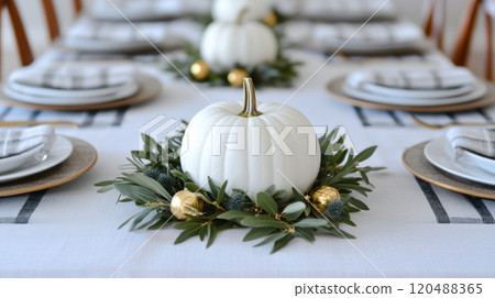 Elegant dining table setting with white pumpkins and greenery centerpiece, soft lighting. 120488365