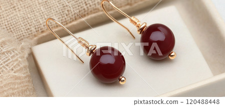 Elegant maroon earrings displayed on a soft fabric background. 120488448