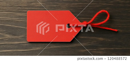 Red tag with a string on a wooden background, ideal for labeling and pricing. 120488572