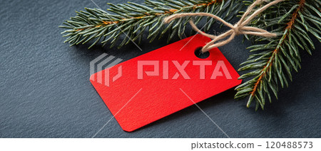 Red tag with pine branches on dark surface, perfect for holiday decoration. 120488573