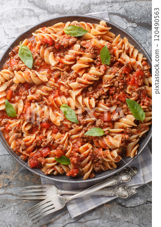 Fusilloni bolognese pasta with a hearty meat tomato sauce closeup on the plate. Vertical top view 120490563