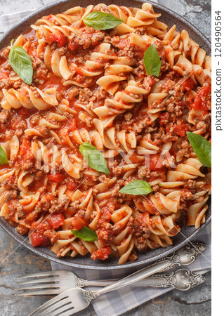 Bolognese pasta Fusilli with tomato sauce, ground minced beef, basil leaves closeup on the plate on the table. Vertical top view 120490564