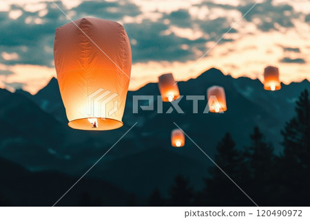 A group of lit candles are floating in the sky above a mountain range 120490972